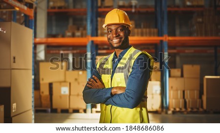 Handsome and Happy Professional Worker Wearing Safety Vest and Hard Hat Smiling with Crossed Arms on Camera. In the Background Big Warehouse with Shelves full of Delivery Goods. Medium Portrait Royalty-Free Stock Photo #1848686086