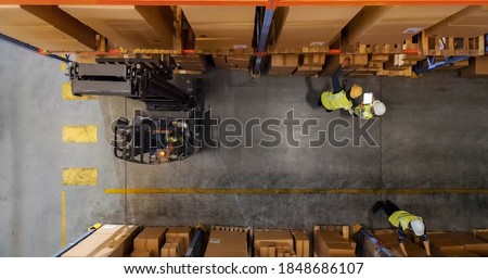 Top-Down Shot: Electric Forklift Truck Operator Lifts Pallet with Cardboard Box of in a Big Retail Warehouse a Shelf. Logistics Product and Goods Delivery and Distribution Center