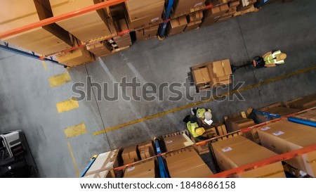 Top-Down View: Worker Moves Cardboard Boxes using Hand Pallet Truck, Walking between Rows of Shelves with Goods in Retail Warehouse. People Work in Product Distribution Logistics Center Royalty-Free Stock Photo #1848686158