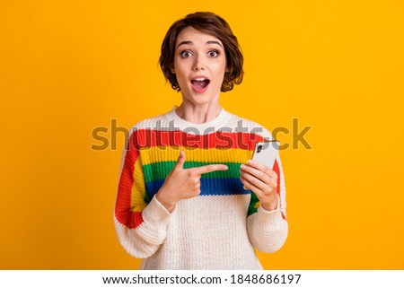 Photo of excited lady hold telephone direct forefinger wear striped pullover isolated yellow color background