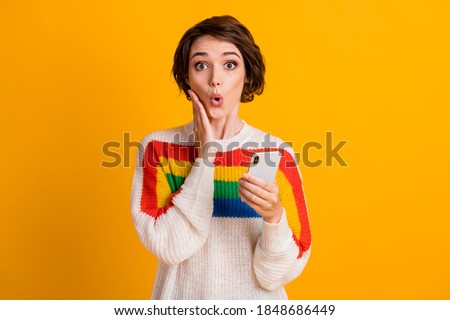 Photo of amazed young lady hold cellphone palm cheekbone crazy face wear striped sweater isolated yellow color background
