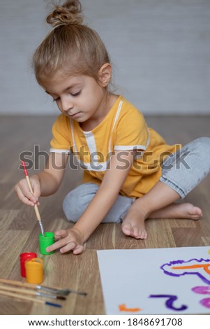 Little preschool child girl sitting on warm floor and painting numbers with paints.