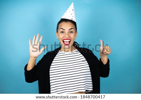 Young beautiful woman wearing a birthday hat over insolated blue background showing and pointing up with fingers number six while smiling confident and happy