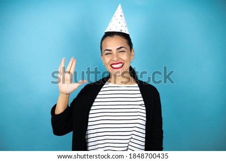 Young beautiful woman wearing a birthday hat over insolated blue background doing hand symbol