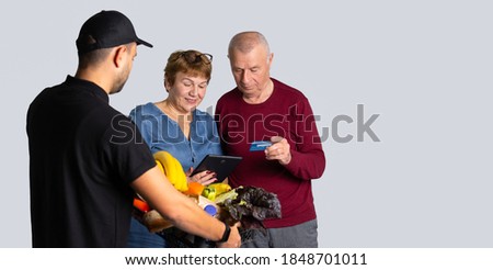 Banner, long format. An elderly family pays for courier delivery by credit card. Photo over white background with empty side space. Senior online concept and pandemic concept