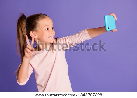 Photo of brown haired tails little girl wear sweater hold phone make selfie v-sign isolated on purple color background