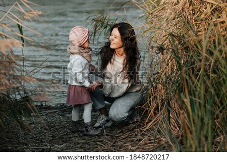 young happy and smiling mother with her little daughter in her arms, hugging and kissing, spending the weekend on a walk in the autumn park.