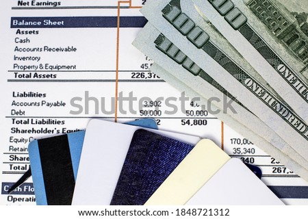 several credit cards along with dollars are on financial documents with numbers.