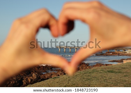 Port Elizabeth Shark Rock pier enclosed by out of focus hands making the shape of a heart. Eastern Cape, South Africa tourism photo. 