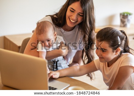 Mother playing with her daughter and baby boy in living room.They using laptop to watch cartoons.	