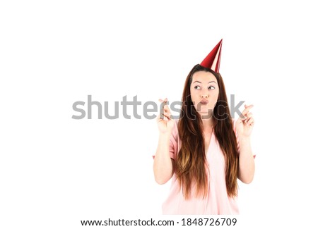 Beautiful young woman crossing her fingers while wearing a red party hat against a white background