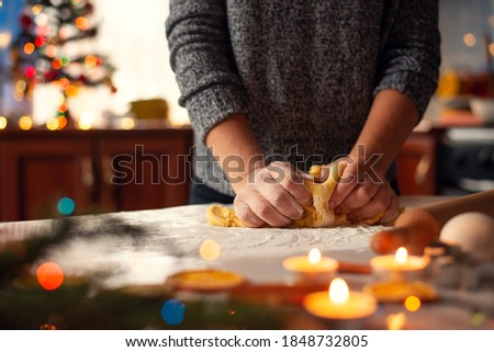 Close-up picture of hands of a girl making dough on the table decorated with christmas candles, lights, cinnamon