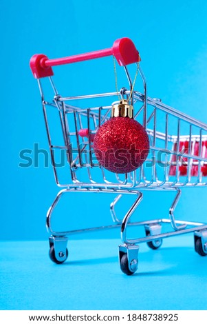 Christmas ball with glitter on the shopping cart against the blue background. Concept of shopping for Christmas presents