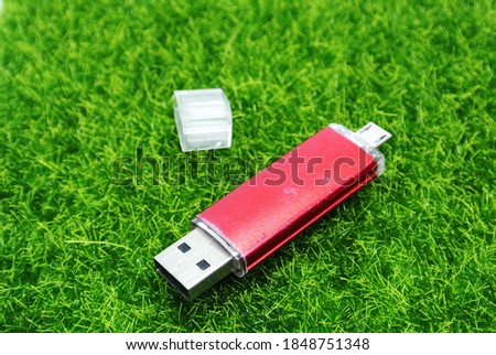 A usb flash drive also known as a USB stick, USB thumb drive or pen drive. USB flash drive with function On The Go (OTG) is famous nowaday. Green grass background. Selective focus.