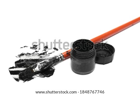Spilled black watercolor with bottle and paintbrush isolated on white background, top view