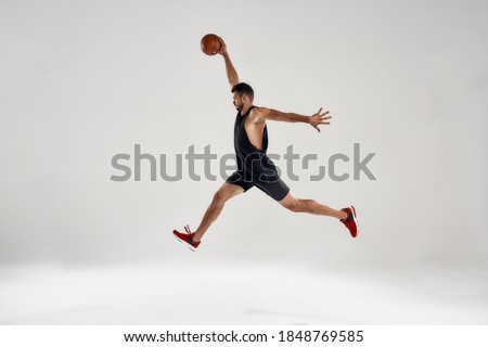 Young handsome caucasian professional basketball player in sideway jump leading ball on gray background. Sports, workout, training concept
