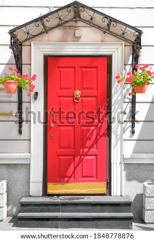 entry door to old house with metallic shelter and flowers. Red entrance door with gold handles. Vintage building facade. Vertical photo