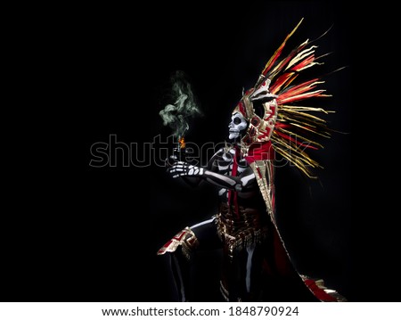 Latin man with death makeup, catrin, dressed as an Aztec god with a clay fret with incense and fire, body paint of bones, a plume of colored feathers and prehispanic costume, day of the dead Royalty-Free Stock Photo #1848790924