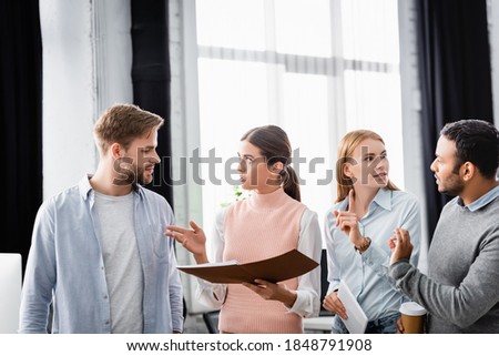 Multiethnic businesspeople gesturing while working with paper folder and digital tablet in office