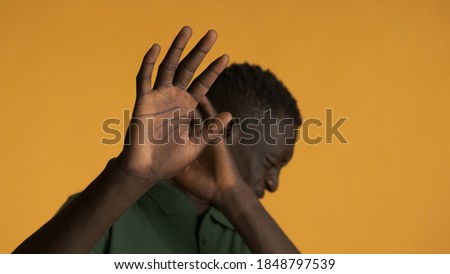 Young afraid African American man scaredly posing on camera over colorful background. Don't want to watch expression