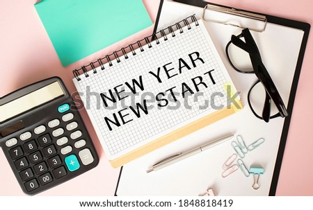 Notepad with NEW YEAR NEW START text on the office table with glasses, calculator, notepad and paper clips.