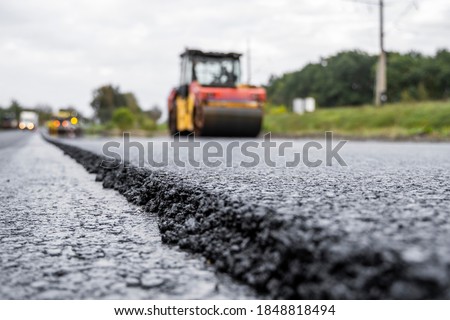 Asphalt road roller with heavy vibration roller compactor press new hot asphalt on the roadway on a road construction site. Heavy Vibration roller at asphalt pavement working. Repairing. Royalty-Free Stock Photo #1848818494