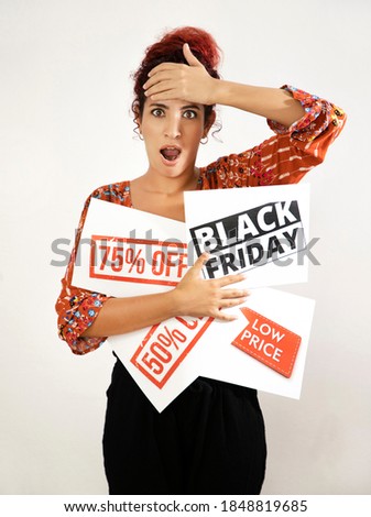 Astonished girl with open mouthed placing one hand on her head and with the other hand holding Black Friday signs, 75% off, 50% off and low prices. Young woman with white skin and curly red hair
