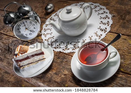 Five o'clock tea. White tea set on an old wooden table with cake, alarm clock and tea strainer. In the style of Alice in Wonderland