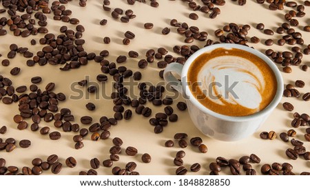 Cappuccino with a beautiful pattern on the milk foam in a white cup on the table cream color and scattered around the roasted coffee beans