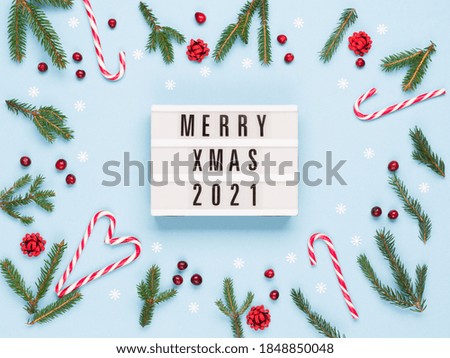 Christmas winter holiday composition. Merry Xmas text on lightbox, Xmas candy canes, Fir tree branches, pastel blue background. Flat lay, top view, copy space. Holiday card mockup template.