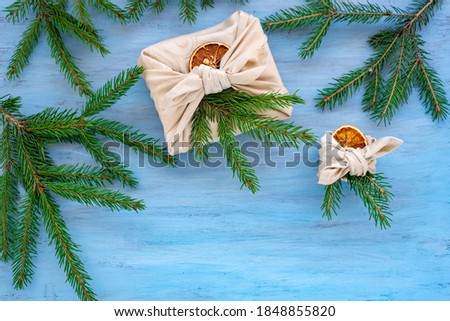 Vertical Christmas card with gifts and Christmas tree branches on blue wooden table. Japanese furoshiki packaging, copyspace