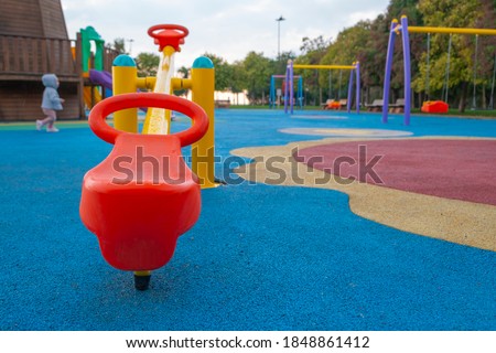 Detail of plastic colored seesaw in children's playground swings in depth of field running small child Royalty-Free Stock Photo #1848861412