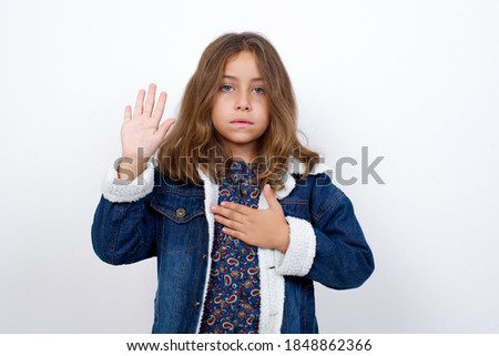 Little caucasian girl with beautiful blue eyes wearing denim jacket standing over isolated white background Swearing with hand on chest and open palm, making a loyalty promise oath