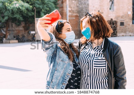 couple of women with a face mask having fun in city taking selfie