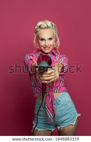 Pin up woman with hairdryer having fun on pink background