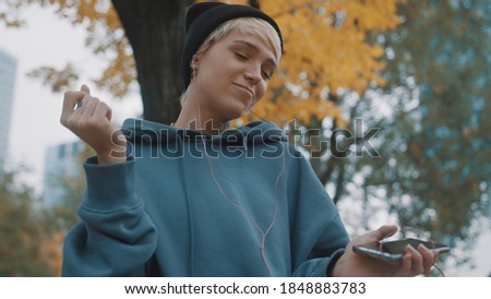 Crazy confident young woman with winter black hat listening to the music from smartphone using earphones in the park. High quality photo