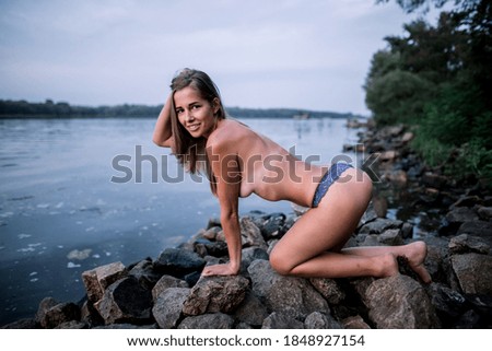 smiling woman in blue panties on the stones by the river