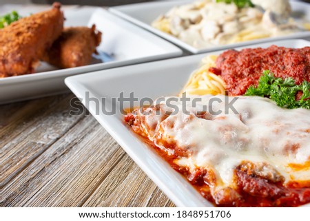 A view of several Italian entrees on a wooden table surface, featuring chicken parmigiana.