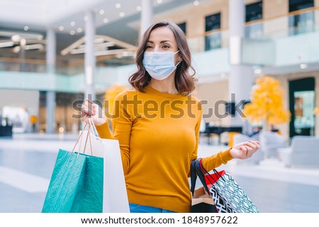 Portrait of casually dressed confident young woman wearing protecting medical mask while walking in mall with bunch of shopping bags in hands. Black friday sales concept. Royalty-Free Stock Photo #1848957622