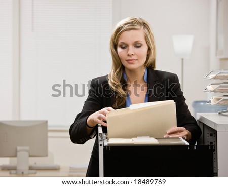 Serious businesswoman searches through file drawer for folder