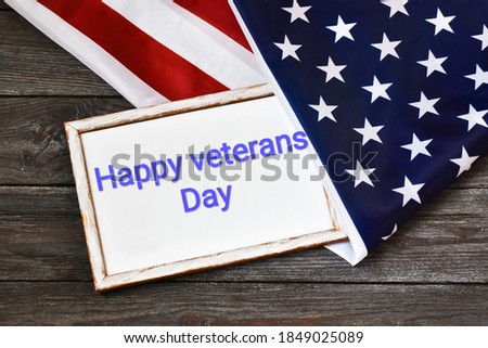 HAPPY VETERANS DAY Text written on chalkboard and flag of the United States on a wooden background. Flat lay.