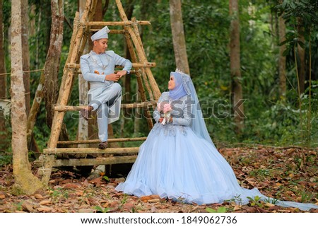 Wedding photo shooting. The bride and groom wearing baby blue  Malay traditional cloth at the forest.