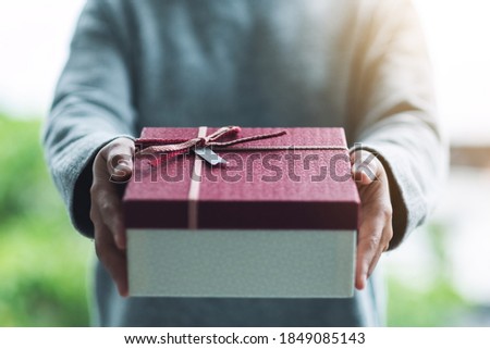 Closeup image of a woman holding and giving a red gift box