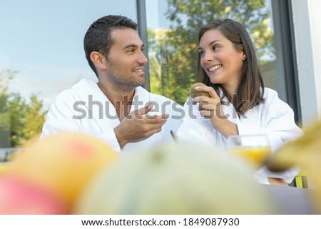Happy young couple in bathrobes having breakfast outdoors