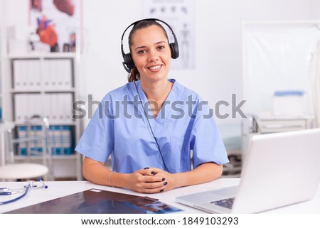 Young practitioner doctor working at the clinic reception desk talking with patients wearing headphones. Female nurse, doctor having a conversation with sick person during consultation, medicine.