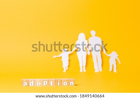 A family cut out of white paper on a yellow background. Wooden cubes with the inscription adoption. Copy space. The concept of adoption