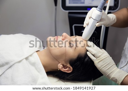 Woman receiving HIFU therapy- high intensity focused ultrasound treatment on face. Therapist doing non-surgical cosmetic plasma lift on client forehead with ultrasonic device. SMAS lifting Royalty-Free Stock Photo #1849141927