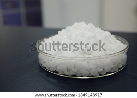 Selective focus of sodium or potassium hydroxide white chemical compound pellets or prills in a petri dish in black background. Royalty-Free Stock Photo #1849148917