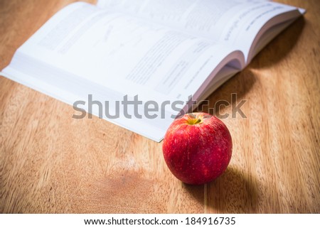 Book and red apple on wood