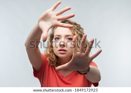 Image of serious blonde girl with curly hair in casual t shirt gestures actively hands at camera, stop gesture with hands. No way, stop doing. Studio shot, white background. Human emotions concept